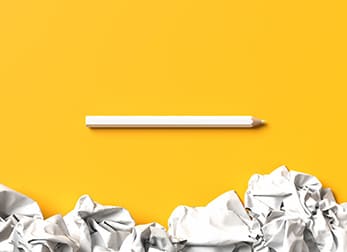 white pencil on top of a yellow background with crushed paper